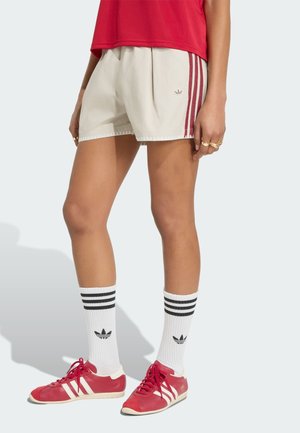 Person iført beige shorts med røde striber, rød skjorte, hvide sokker med sorte striber og røde sneakers med hvide detaljer.