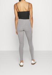 Grå leggings med sidosträckta vita ränder, tillverkade av elastiskt material, i kombination med en svart croppad topp. Outfiten har tunna axelband och en figurnära design.