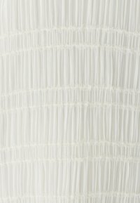 Witte jurkstof met horizontale smocking met gestructureerde plooien en delicate kantafwerking tussen de rijen, wat een gelaagd effect creëert.