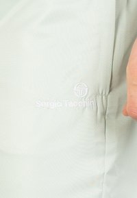 Hellgrüner, strukturierter Stoff mit einem dezenten Diamantmuster. Am Rand befindet sich ein weißes gesticktes Logo von "Sergio Tacchini".