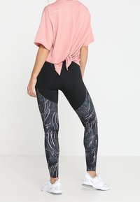 Leggings negros con un diseño estampado que presenta remolinos y puntos; combinados con una camiseta rosa de mangas cortas. Zapatillas deportivas blancas.