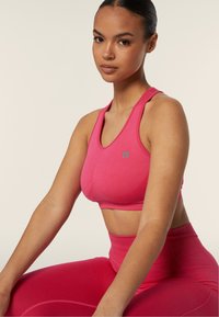 Sostegno sportivo rosa realizzato in tessuto elasticizzato con un design senza cuciture. Presenta un piccolo logo sul davanti e uno stile a schiena incrociata.