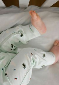 Ljust gröna pyjamasbyxor med ögon- och insektmönster; har en dragkedja och mjukt tyg; en liten fot syns från botten.