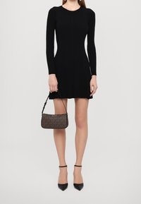 Czarna, prążkowana sukienka z długim rękawem, w połączeniu z małą, brązową torebką w wzory. Czarne sandały na obcasie dopełniają stylizację.