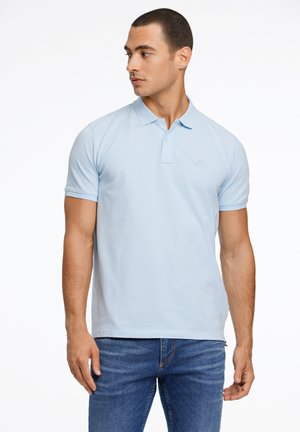 Lyseblå polo med klassisk krave og korte ærmer. Har et subtilt logo på brystet. Båret med mørke denimjeans.