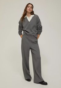 Maglione oversized grigio con scollo a V e colletto bianco, abbinato a pantaloni larghi grigi e mocassini neri. Finitura in tessuto morbido.