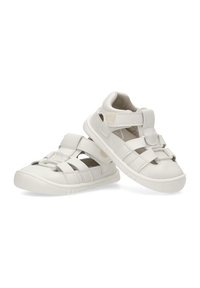 Las sandalias blancas para niños presentan un diseño de varios tirantes, punta cerrada, cierre de Velcro y una suela de goma texturizada para mayor agarre.