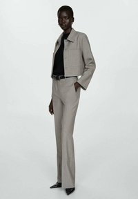 Giacca grigia chiara, cropped, con tre bottoni, abbinata a pantaloni slim-fit. Top nero sotto, tacchi alti neri completano l'outfit.