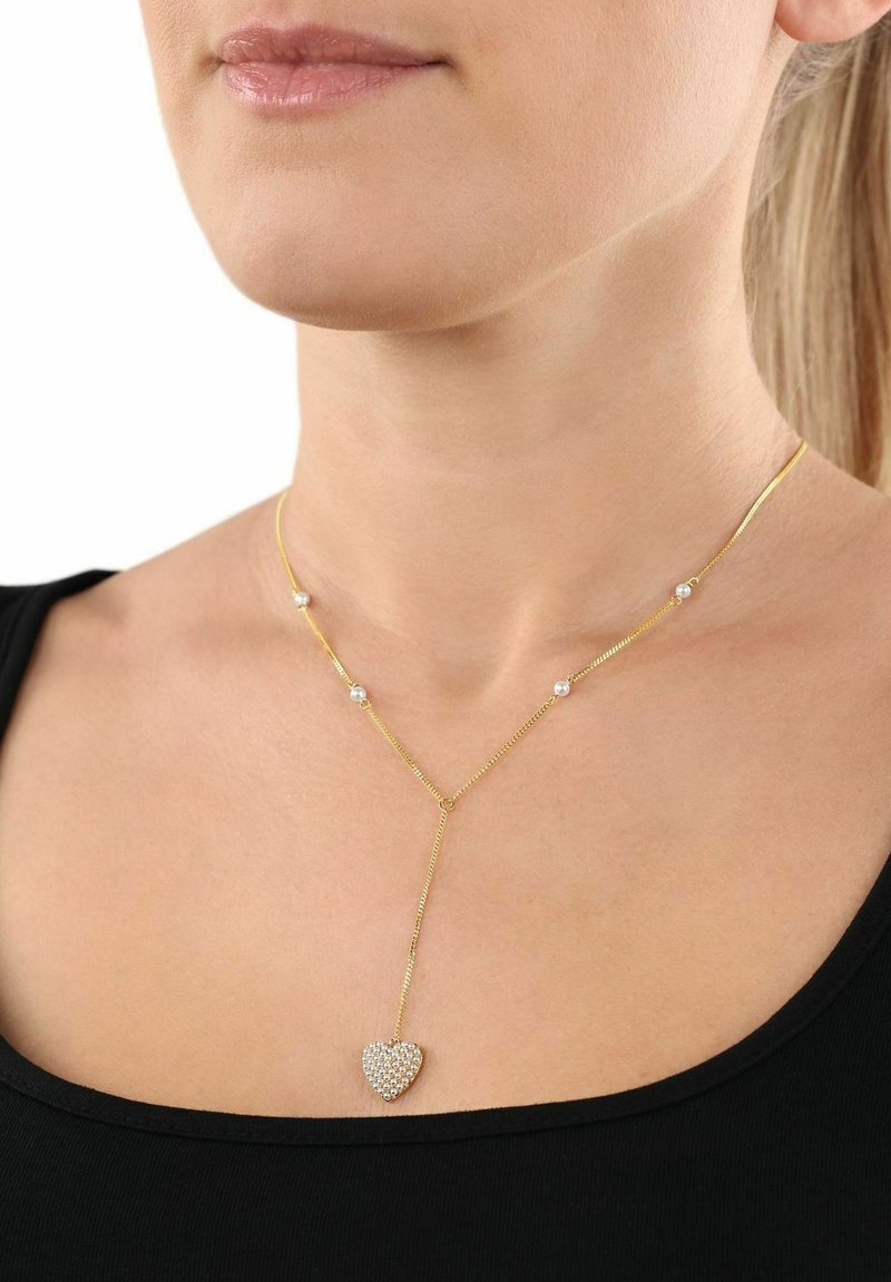 Y-formad guldkedja med ett hjärtformigt hänge prytt med gnistrande klara stenar och små runda detaljer längs kedjan.