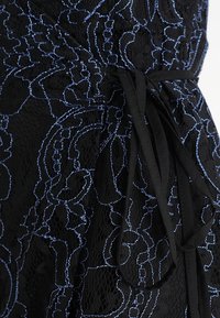 Svart spetstyg med blå floral broderi, med en knytbar midja. Texturerad design med intrikata mönster och en slät yta.