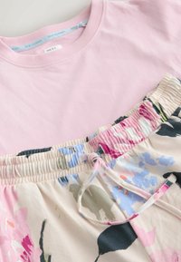 Top roz deschis cu mâneci scurte și guler rotund, peste pantaloni scurți crem cu model floral, prevăzuți cu talie elastică și șnur.