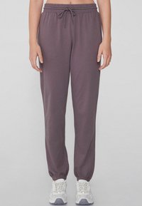 Pantalones deportivos morados con un acabado texturizado, que cuentan con una cintura elástica y dobladillos ajustados. Combinados con zapatillas deportivas gris claro.
