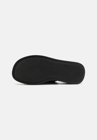 Semelle de baskets noire présentant une surface en caoutchouc texturé, une forme incurvée et un logo de marque en relief sur le côté. Bords lisses et design simple.