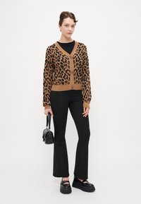 Leopard-patterned cardigan in brown and black, featuring a V-neck, button closure, and ribbed cuffs, paired with black flared pants and platform shoes.