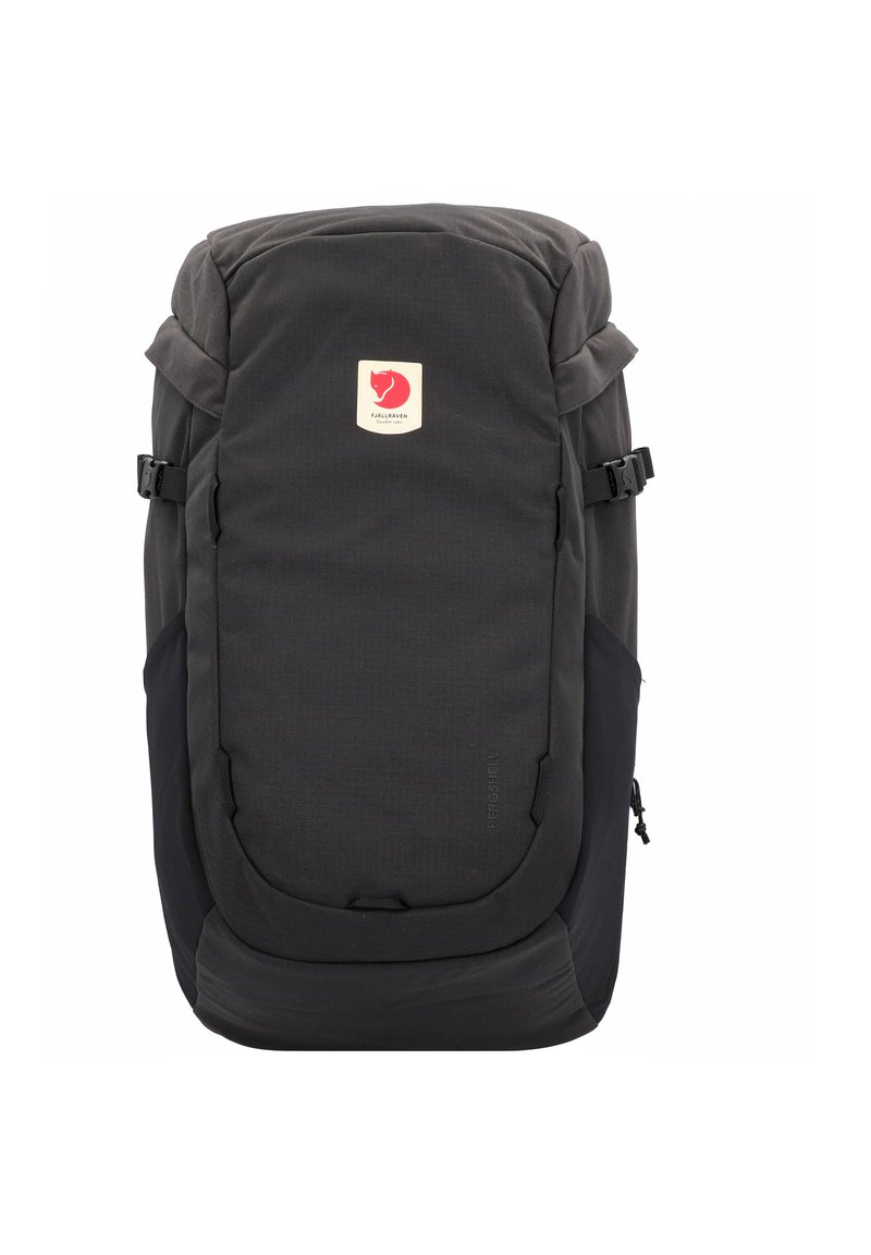Černý látkový batoh s horním klopou, nášivkou s logem, bočními kompresními popruhy a texturovaným povrchem. Obsahuje kapsy na zip a ergonomický design.