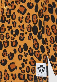 Leopardenmusterstoff in warmem Orange, mit schwarzen und braunen Flecken. Beinhaltet ein weißes Etikett mit einer Panda-Grafik, der einen Zylinder trägt.