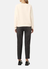 Jasno-beżowy sweatshirt o luźnym kroju z prążkowanymi mankietami, połączony z ciemnoszarymi jeansami slim-fit i czarnymi, masywnymi butami. Gładka struktura.