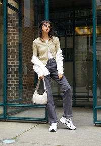 Beige ribbatut jakke over en hvit topp, grå jeans, og hvite joggesko. Grå veske med en buet form og myk tekstur. Briller fullfører stilen.