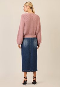 Miękki różowy sweter wykonany na drutach z opadającymi ramionami i ribbowaną teksturą, zestawiony z niebieską spódnicą dżinsową z przetarciami i średniej długości krojem.