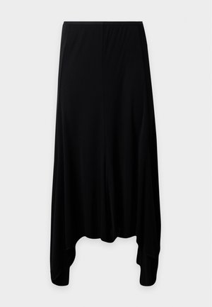 Woman standing wearing a black V-neck top with three-quarter sleeves and an asymmetrical black midi skirt with beige pointed heels.