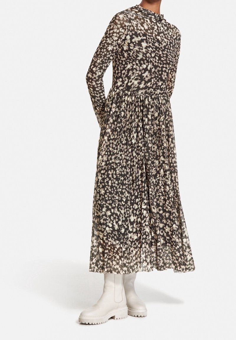 Langærmet, tiered kjole i gennemsigtigt stof med blomsterprint i creme og taupe på en mørk baggrund, parret med hvide chunky støvler.