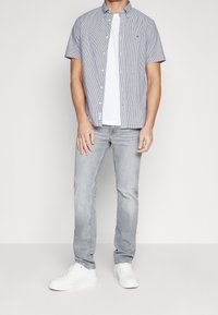 Camicia a maniche corte con bottoni, a righe blu e bianche, abbinata a una t-shirt bianca semplice e jeans grigi chiari, completata da sneaker bianche.