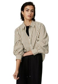 Gestreepte button-up blouse in crèmekleur en bruin. Kenmerkt zich door een relaxte fit, met pofmouwen en een klassieke kraag. Gemaakt in combinatie met een zwarte onderkant.