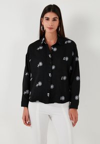 Black long-sleeve shirt with white floral pattern, buttoned front, and a collared neckline. Soft texture and relaxed fit.
