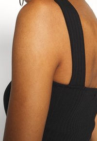 Svart randig linne med breda axelremmar och en figurnära design, som visar en texturerad tyg och en låg rygg.