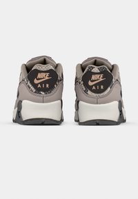 Sneakers Nike Air con tomaia grigia, dettagli in motivo serpente strutturato e suola in gomma nera. Presentano il logo Nike sul tallone.