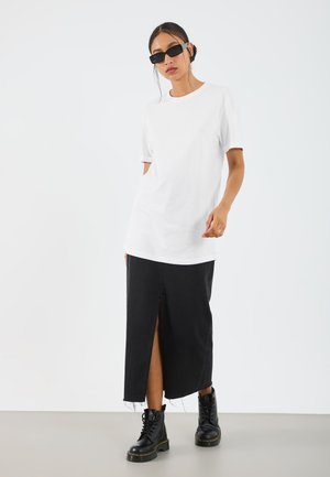T-shirt blanc en coton à manches courtes associé à une jupe maxi en denim noire avec une fente devant et un ourlet effiloché, portée avec des bottes noires à lacets.