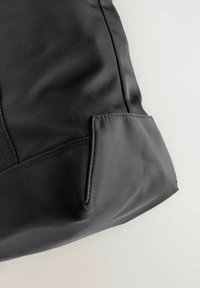 Schwarze Stofftasche mit glatter Textur, ausgestattet mit einer kleinen Außentasche und gesteppten Details. Das Design ist schlicht und klar.