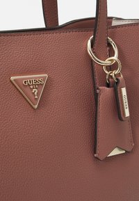 Geantă tote din piele texturată, de culoare maro, cu detalii din metal auriu, badge-logo în formă de triunghi și un tag cu numele brandului.