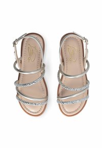 Sandalias plateadas con tiras cruzadas, que presentan acentos metálicos y de rhinestones, sobre una plantilla beige y suela marrón. Hebilla ajustable.