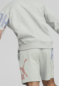 Sudadera gris claro con un gráfico multicolor en la manga, combinada con pantalones cortos grises claros que presentan un estampado de logo en acentos rojos y azules.