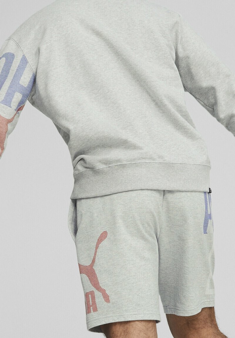 Sudadera gris claro con un gráfico multicolor en la manga, combinada con pantalones cortos grises claros que presentan un estampado de logo en acentos rojos y azules.