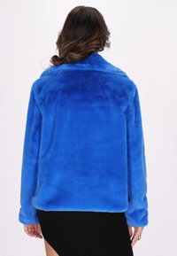 Giacca in pelliccia sintetica di un blu vivace, con una texture morbida, una vestibilità rilassata e un ampio colletto. L'orlo arrotondato e le maniche lunghe aggiungono comfort.