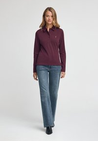 Mörkröd långärmad polo med krage och tre knappar, i kombination med ljusblå vida jeans och svarta ankelstövlar.