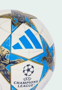 Hvid og blå UEFA Champions League fodbold med guld løve- og edderkopillustrationer samt Adidas-logo på de viste paneler.