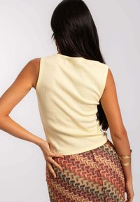 Top sin mangas amarillo con un diseño ajustado. Combinado con una falda estampada que presenta motivos geométricos en rojo, marrón y beige.