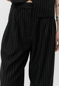 Tailored black pants with vertical white pinstripes, pleated front, and a smooth texture. Features a matching belt and side pockets.
