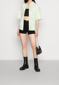 Camiseta teñida de verde claro, top corto negro, shorts negros y botines negros. Lleva un pequeño bolso negro con cadena plateada.