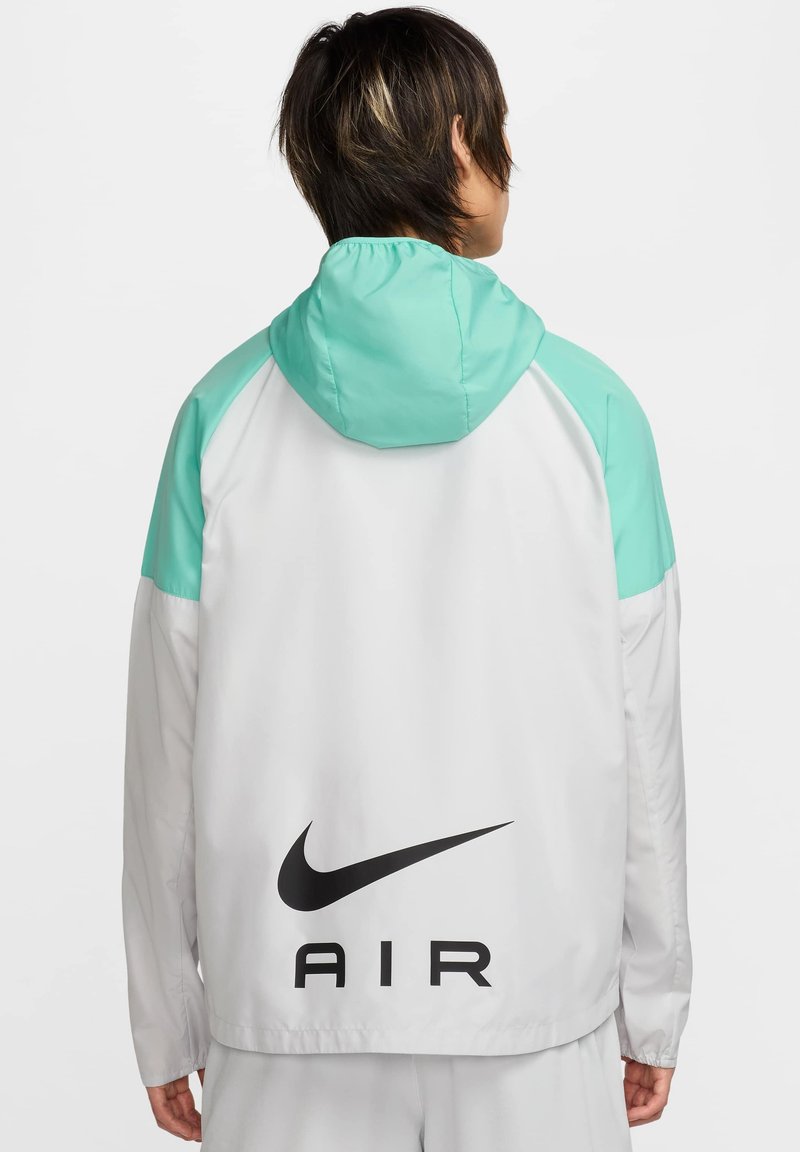 Kurtka lekka z turkusowym kapturem i akcentami na ramionach, biała korpus i duże czarne logo "Nike AIR" na dolnej części pleców.