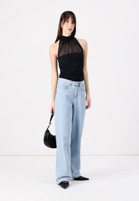 Crna halter top majica s prozirnim detaljima, uparena s svijetlo plavim širokim trapericama i crnim salonkama. Uključena je crna torba.