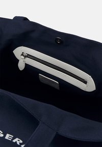 Navy niebieska torba tote z wnętrzem z białą kieszenią na zamek błyskawiczny. Srebrny zamek i skórzana pętla. Solidna tekstura materiału, bezpieczne zapięcie na zatrzask.