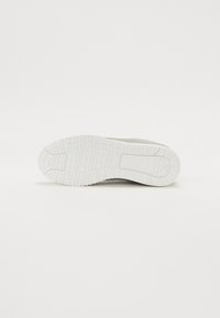 Semelle de sneaker blanche avec une gomme texturée, présentant un grip à motifs et un design de talon plat pour une traction et une stabilité.