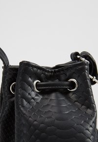 Czarna skórzana torebka typu bucket z fakturowanym, łuskowatym wzorem. Posiada zamknięcie na ściągacz z srebrnym okuciem oraz pojedynczy pasek na ramię.