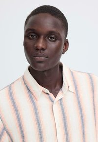 Hemd met kraag van licht materiaal, voorzien van verticale strepen in perzik, crème en blauw. Knopen bij de halslijn, met een gestructureerde weving.