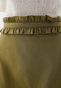Olijfgroene rok met een geraffineerde tailleband, gemaakt van textuurstof. Close-up van het ontwerp van de tailleband en de stikdetails.