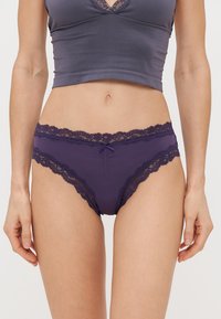 Fialové kalhotky s krajkovým okrajem, vyrobené z měkké látky, středního výřezu, a s dekorativní mašličkou vpředu, zdůrazňující jemné krajkování.